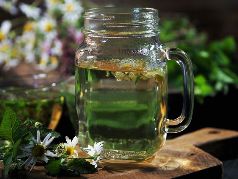 čaj od kamilice u šoljici i u teglici za piće, pored kamilica
