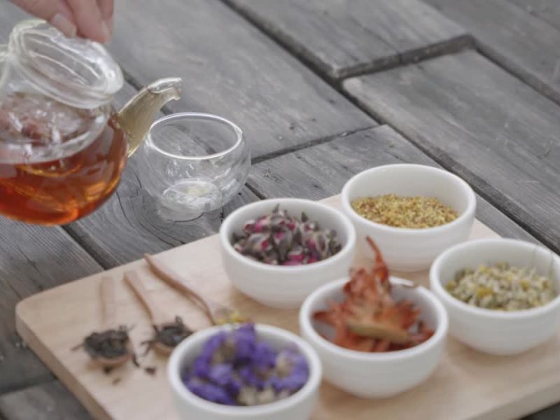 par sušenih biljaka u činijicama i čaj pored koji se sipa iz čajnika