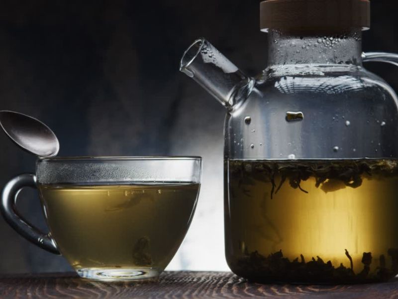 prikaz staklenog čajnika punog biljnog čaja i šoljice pune čaja sa kašičicom